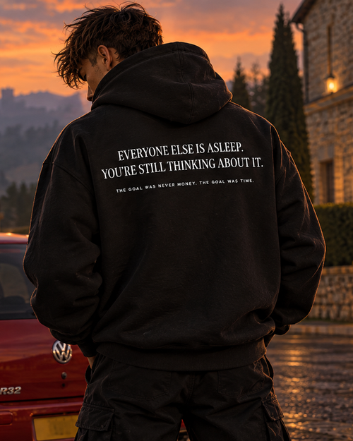 Back of the black UNSETTLED Core Hoodie on a model, printed in white: Everyone else is asleep. You’re still thinking about it.